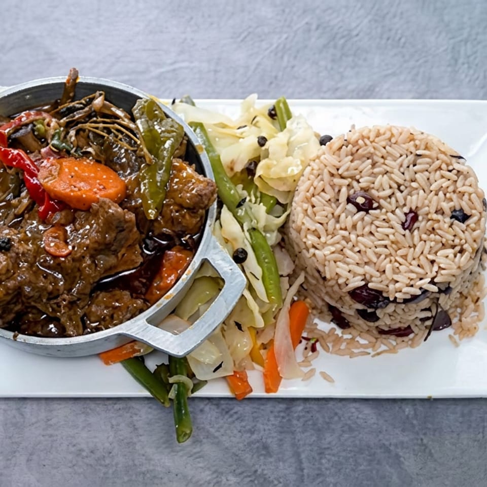 Stewed meat with peppers and vegetables in a small skillet, served alongside a dome of rice and beans on a white plate.