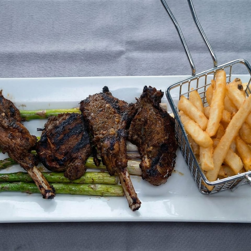 Grilled lamb chops and asparagus served on a white plate with a basket of golden French fries.