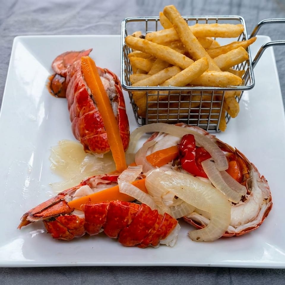 Platter of lobster, shrimp, onions, and carrots served with golden fries in a small wire basket.